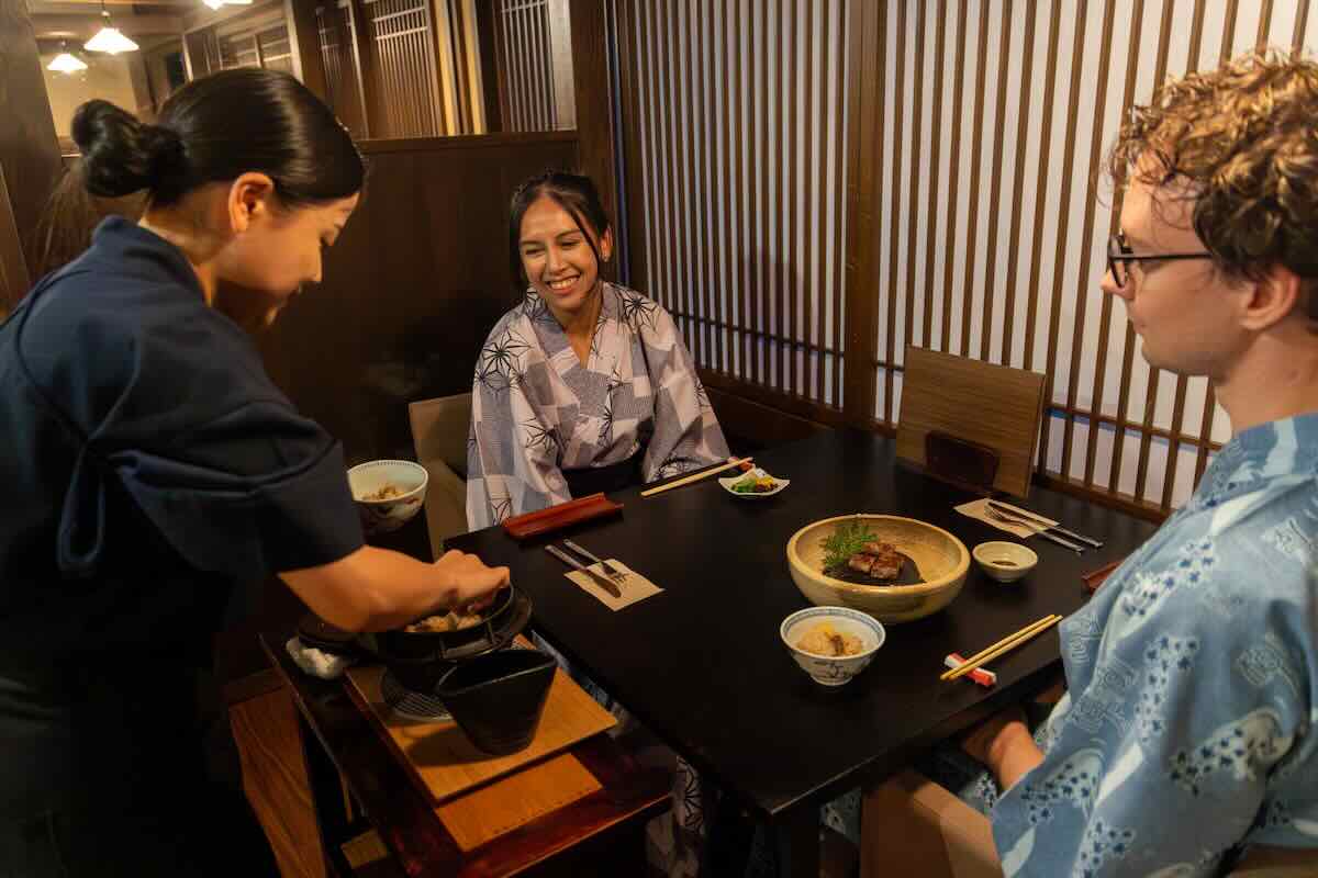 Staff serving a traditional Japanese dinner to guests wearing yukata at Kashiwaya Ryokan in Shima Onsen