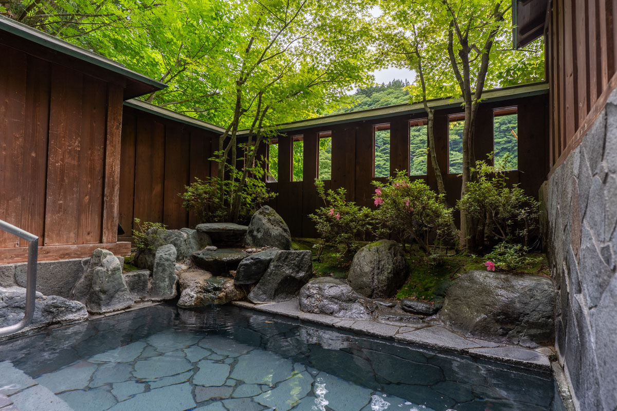 Private outdoor onsen bath surrounded by fresh greenery at Kashiwaya Ryokan in Shima Onsen